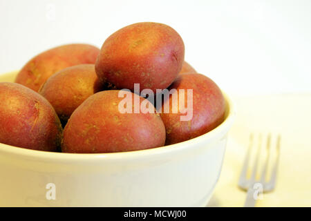 Una ciotola di patate novelle rosse si siede contro uno sfondo bianco con una forcella sfocata accanto ad essa. Foto Stock