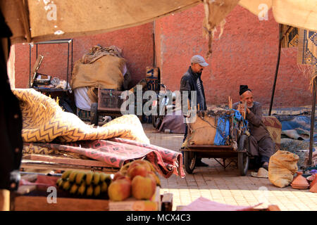 Senior uomo vendita di tappeti ed altri tessuti sul vecchio souk nel quartiere della Medina di Marrakech, Marocco Foto Stock