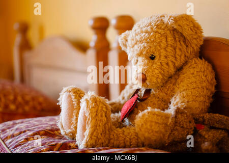 Triste di fronte orsacchiotto seduto da solo su un letto. La illustra la solitudine e la depressione Foto Stock