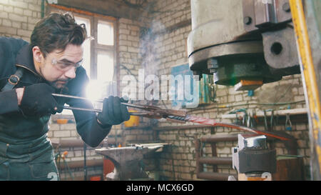 L'uomo fabbro in officina di un rosso di forgiatura ferro caldo sull'incudine - small business Foto Stock