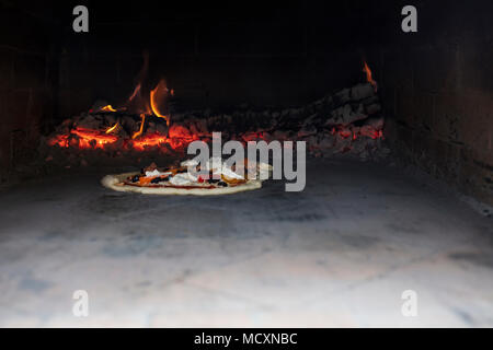 La Pizza La cottura in un forno esterno con la combustione del legno in background Foto Stock