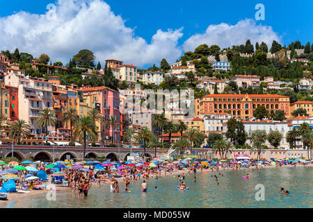 La gente sulla spiaggia pubblica come vecchie case colorate su sfondo a Menton - piccola cittadina sulla Riviera Francese. Foto Stock