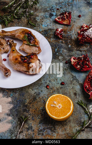 Deliziose grigliate di cosce di pollo con semi pomegranade e arancione sulla superficie di cemento Foto Stock