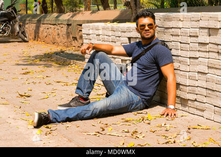 Giovane ragazzo che indossa jeans e maglietta si siede e posa Foto Stock