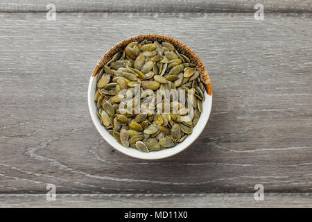 Tabella vista dall'alto sulla piccola ciotola di vetro pieno di caffè tostato salati semi di zucca sul grigio di una scrivania di legno. Foto Stock