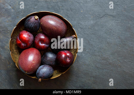 Dark frutti esotici su sfondo di ardesia compresi il frutto della passione, prugne, fichi, con spazio copia a destra Foto Stock