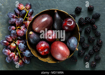 Dark frutti esotici su sfondo di ardesia compresi il frutto della passione, prugne, fichi, uva e bacche nere Foto Stock