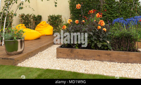 Luminose colorate di piante fiorite in letti di legno e giallo sedie beanbag su decking - "Il viaggio Garden' - RHS Flower Show, Tatton Park, England, Regno Unito Foto Stock