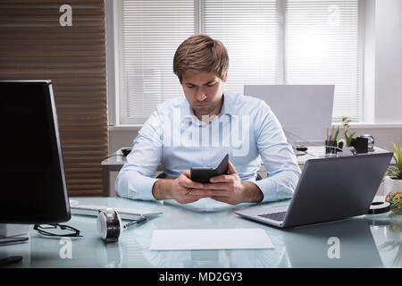 Giovane Imprenditore seduto in ufficio utilizzando il telefono cellulare Foto Stock