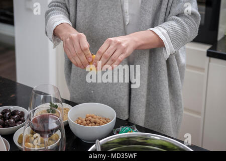 Close-up di donna spremendo il limone su peaspreparation pulcino di hummus classico. Foto Stock