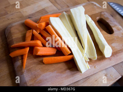 Tritate le carote affettate e pastinaca sul tagliere di legno in cucina Foto Stock