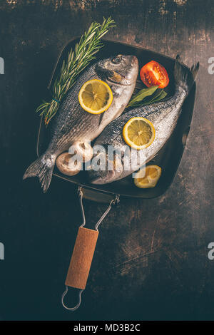 Vista superiore del pesce con spezie e verdure in teglia su sfondo irregolare. Foto Stock