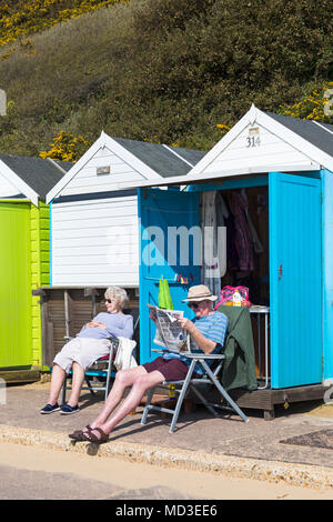 Bournemouth Dorset, Regno Unito. Il 18 aprile 2018. Regno Unito: meteo bella calda giornata di sole a Bournemouth spiagge con cielo azzurro e sole ininterrotta, come i visitatori in testa al mare per godere il giorno più caldo dell'anno finora. Coppia matura relax da loro beach hut - uomo leggendo il quotidiano. Mini ondata di caldo. Credito: Carolyn Jenkins/Alamy Live News Foto Stock