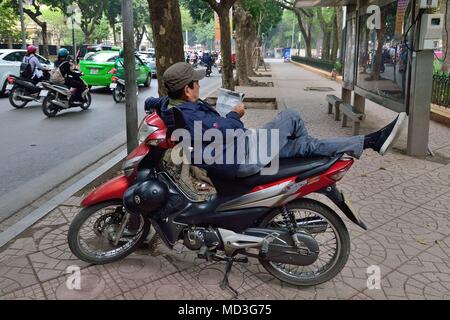 Hanoi, Vietnam. Xv Apr, 2018. Un uomo con una moto come una sedia a sdraio per leggere il suo giornale di Hanoi, Vietnam. Credito: Rory Merry/ZUMA filo/Alamy Live News Foto Stock