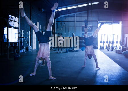 Tre persone che esercitano in palestra, due uomini facendo passeggiate handstand Foto Stock