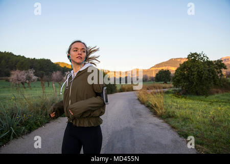 Giovane donna in corsa lungo la strada rurale, indossando il tracker di attività Foto Stock