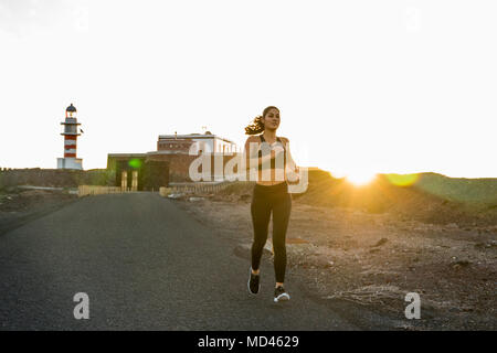 Giovani femmine runner correndo giù per strada rurale al tramonto, Las Palmas, Isole Canarie, Spagna Foto Stock
