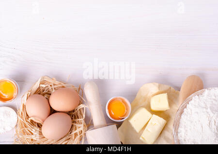 Ingredienti per la cottura croissant - farina, il cucchiaio di legno, mattarello, le uova e i tuorli, burro servita su sfondo bianco. Foto Stock