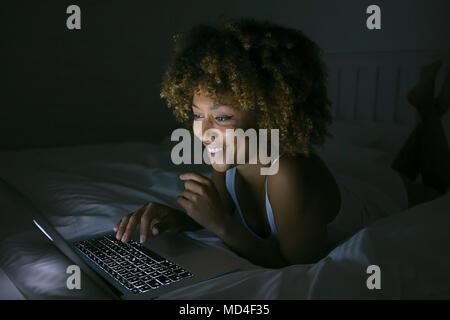 Donna sorridente chiacchierando con il computer portatile nel buio Foto Stock