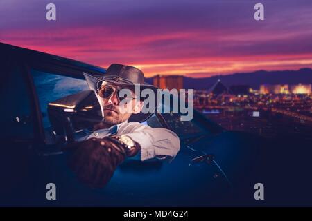 Cowboy lasciando a Las Vegas. Uomini caucasici nella sua 30s nella parte occidentale di usura e cappello da cowboy dentro il suo classico Muscle Car Ride. Foto Stock