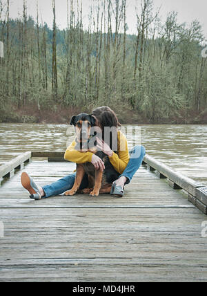 Una donna e il suo cane seduto su di un molo di Oregon. Foto Stock