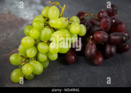 Grappoli di uva uva verde e uva rossa seduta su un flaylay grigio Sfondo testurizzata Foto Stock
