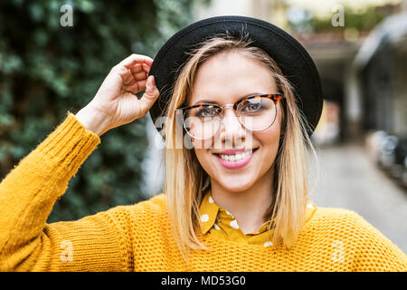 Giovane donna con cappello nero e degli occhiali nella soleggiata città di primavera. Foto Stock