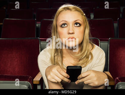 Una giovane donna con il suo telefono cellulare in un cinema. Foto Stock