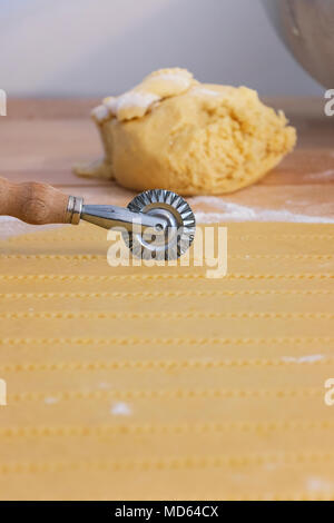 Pasticceria ruota di coltello taglia un strato di pasta sfoglia , in sfondi un impasto crudo con farina, in primo piano le linee di pasticceria fuori fuoco Foto Stock