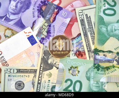 MONTREAL, Canada - 10 Marzo 2018: Ethereum cryptocurrency moneta in oro e logo su euro e dollari americani e dollaro canadese di banconote. Foto Stock