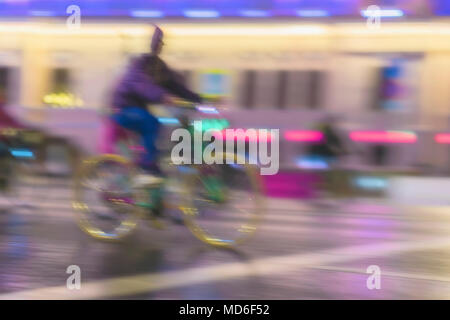 Giovane biker equitazione Bicicletta durante la notte su una strada di città, scena urbana. Abstract sfocato background moderno Foto Stock
