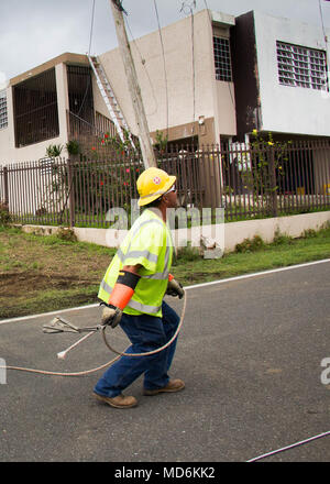 Un lavoratore di linea lancia una corda guida su un cavo esistente. Egli potrà utilizzare la fune per tirare una nuova linea attraverso la strada.il lavoro degli equipaggi di riparazione delle linee elettriche in una cima comunità in Naranjito. Come del 26 marzo 2018, oltre il 94 percento dei clienti in Puerto Rico hanno Alimentazione ripristinata. Il restante 6 per cento sono situati principalmente nelle aree montane. Nonostante il trasporto e sfide di accesso, il lavoro degli equipaggi sull isola si stanno concentrando i loro sforzi in queste aree remote, con l obiettivo di raggiungere il 95% di restauro in queste regioni entro la fine di maggio. Foto Stock