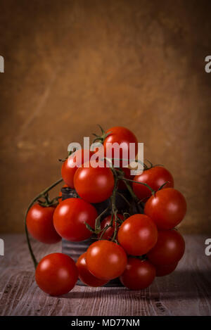 Foto verticale con pochi ramoscelli piena di piccoli rossi pomodori ciliegia. Vegetale è collocato in usurata può vintage. Lo stagno è sulla tavola di legno con bianco e marrone Foto Stock