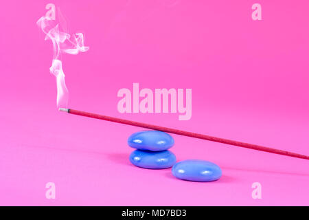 Stick di Incenso che brucia e il fumo sulla roccia blu su sfondo rosa in studio Foto Stock