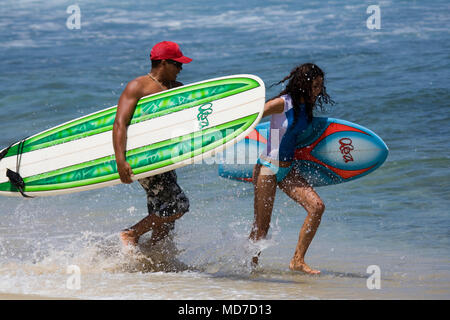 L uomo e la donna, corsa sulla spiaggia tenendo le tavole da surf Foto Stock