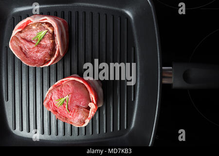 Raw bistecca di manzo con pancetta e rosmarino in padella per grigliare vista dall'alto. Il cibo gustoso background. Foto Stock