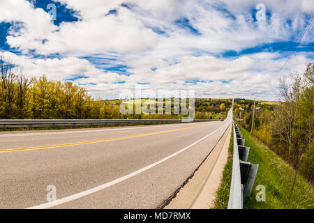 Strada aperta nella zona rurale mostra lunga strada pavimentata con splendido cielo blu e nuvole bianche Foto Stock