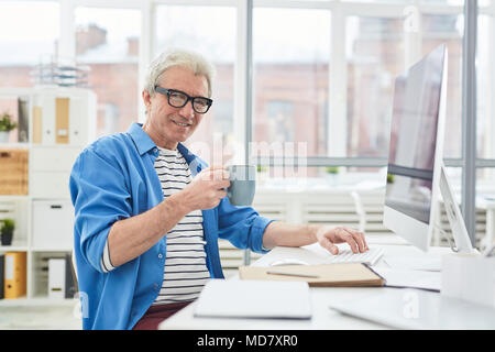 Ritratto di senior executive seduto al tavolo di office e di bere il tè Foto Stock