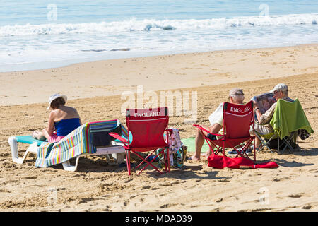 Bournemouth Dorset, Regno Unito. Il 19 aprile 2018. Regno Unito: meteo bella calda giornata di sole a Bournemouth spiagge con cielo azzurro e sole ininterrotta, come i visitatori in testa al mare per godere il giorno più caldo dell'anno finora. Due uomini leggendo quotidiani sulla spiaggia, una seduta sulla sedia in Inghilterra e la donna rilassante sul lettino. Credito: Carolyn Jenkins/Alamy Live News Foto Stock