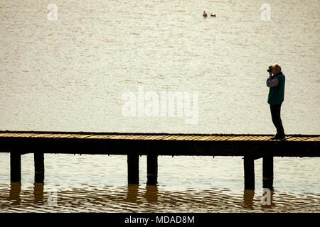 Una persona in piedi su un pontile in legno presso la popolare località balneare di Llandudno scattare una foto silouetted contro la marea, Llandudno, Wales, Regno Unito Foto Stock