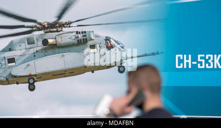 19 aprile 2018, Schönefeld, Germania: un lavoratore passeggiate passato una foto del nuovo Sikorsky CH-53K heavy-duty elicottero sul motivo del Salone internazionale aerospaziale ILA. L'elicottero ha la sua premiere mondiale a una mostra con la ILA. Presso la ILA 2018 circa 200 aeromobili sono destinati a essere presentati. Gli organizzatori si aspettano più di 150.000 visitatori. La Ila avviene dal 25 aprile al 29 2018. Foto: Ralf Hirschberger/dpa Foto Stock