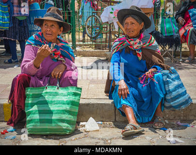 Due senior donne indigene del Tarabuco minoranze indigene in chat e parlare, seduto sul marciapiede, sul mercato di domenica, Tarabuco, Bolivia Foto Stock