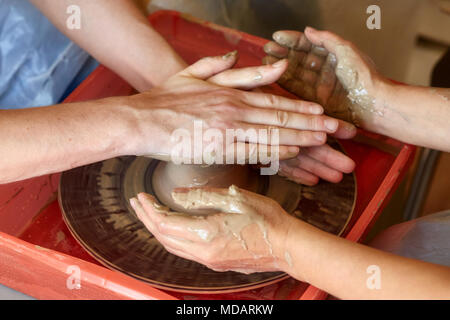 Le mani di due persone creare vaso sul tornio del vasaio. Insegnamento in ceramica, carftman con le mani in mano la guida Foto Stock