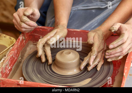 Le mani di due persone creare vaso sul tornio del vasaio. Insegnamento in ceramica, carftman con le mani in mano la guida Foto Stock