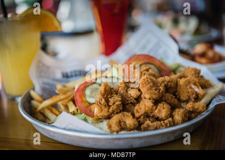 Popcorn Shrimp fritta ricoperta di cocco con pastella, servito sul vassoio di alluminio con fruttato bevande tropicali in background. Foto Stock