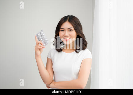 Persone, bellezza, salute e medicina concetto - felice giovane donna azienda confezione di pillole in camera Foto Stock