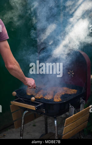 Irriconoscibile man mano girando le bistecche di maiale su un barbecue a carbone Foto Stock