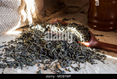 Il tè verde cinese. Cumulo di foglie di tè sulla trama tovaglie di lino con bambù cucchiaio. Aromatico e bibita salutare ampiamente utilizzato in tutto il mondo. Foto Stock