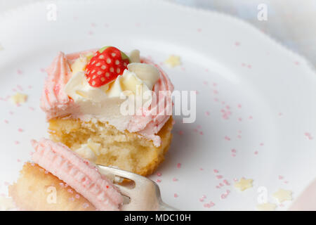 Fragola Rosa cupcake sulla piastra bianca con star spruzza essendo mangiato Foto Stock