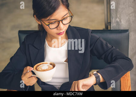 Smart Asian business woman holding mocha latte art caffè e cercando guarda il tempo. Foto Stock